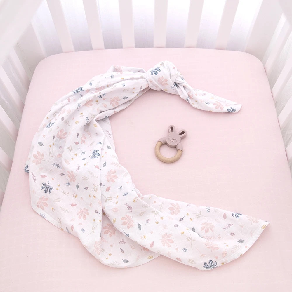 organic muslin pink botanical leaf design baby swaddle with silicone and wooden bunny teether in cot.