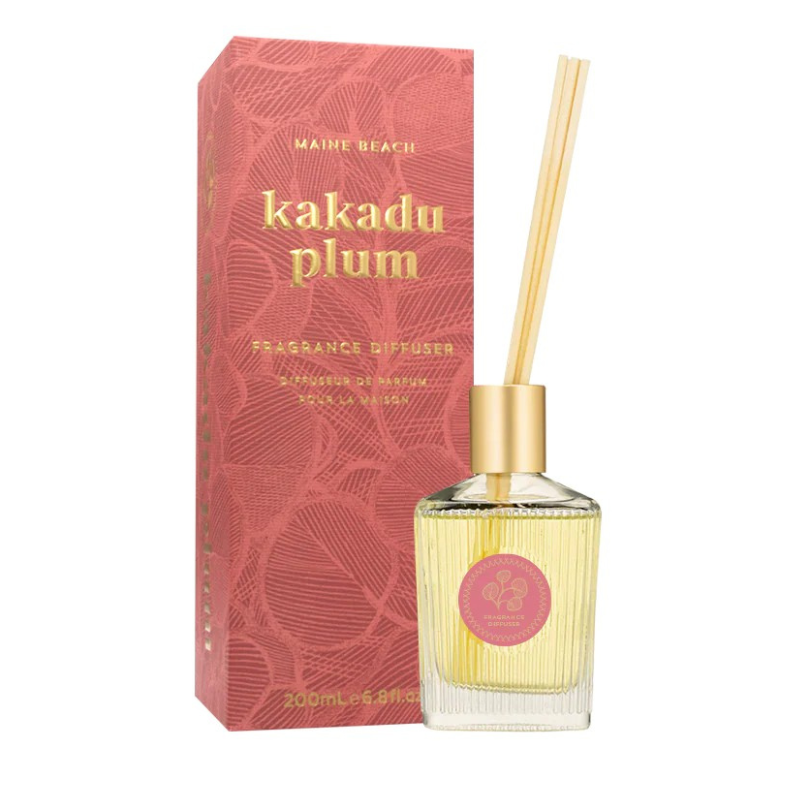 Fragrance diffuser bottle with pink label and gold cap next to its packaging on a white background