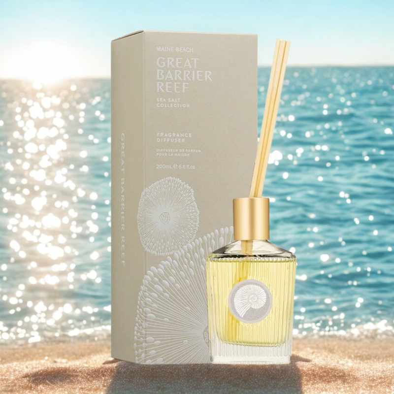 Diffuser bottle with gold cap and packaging labeled 'Great Barrier Reef' on a beach.