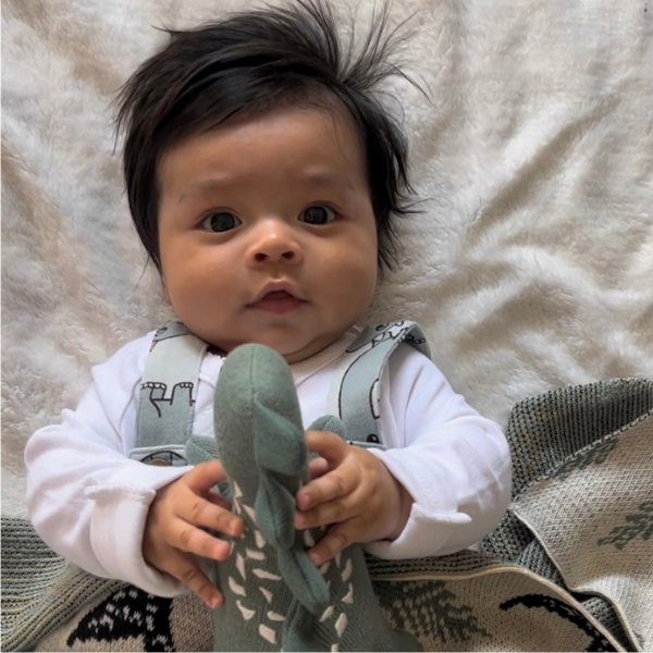 baby wearing dinosaur overalls under a baby blanket