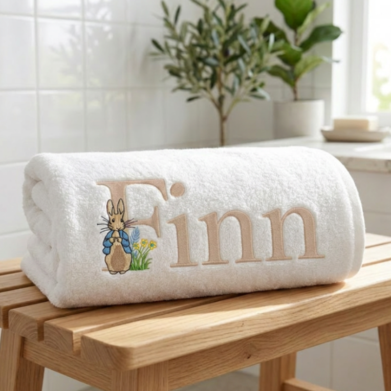 White towel with embroidered name 'Finn' in a latte colour and a rabbit design on a wooden surface.