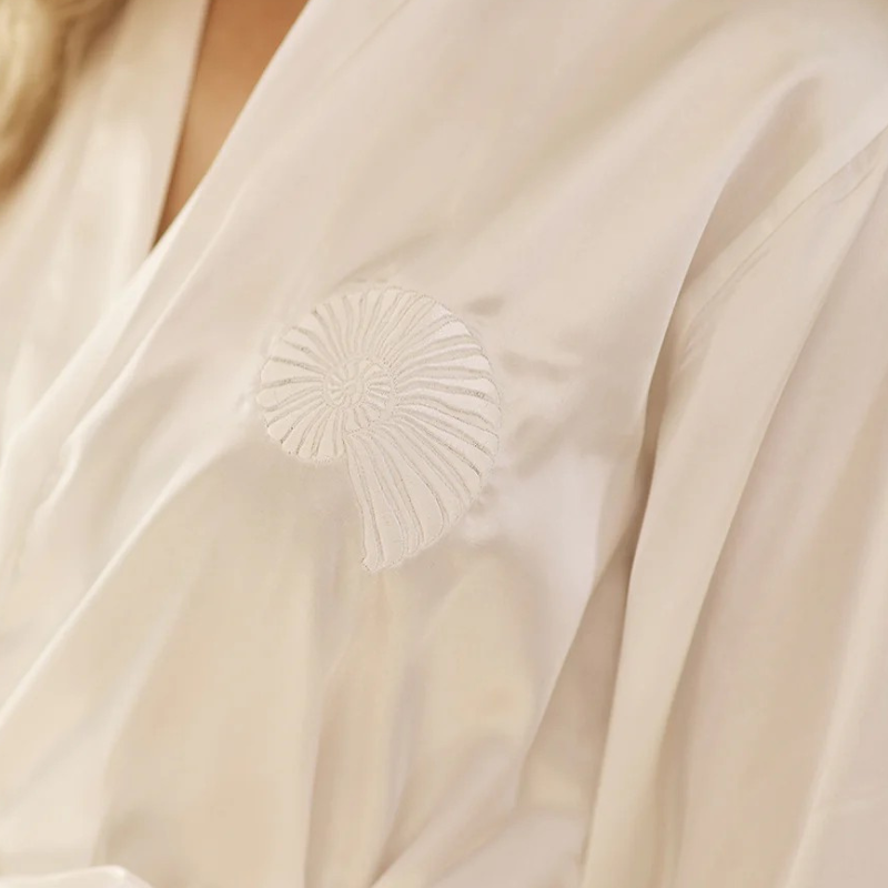 Close-up of a womans white satin gown robe with a subtle embroidered shell pattern