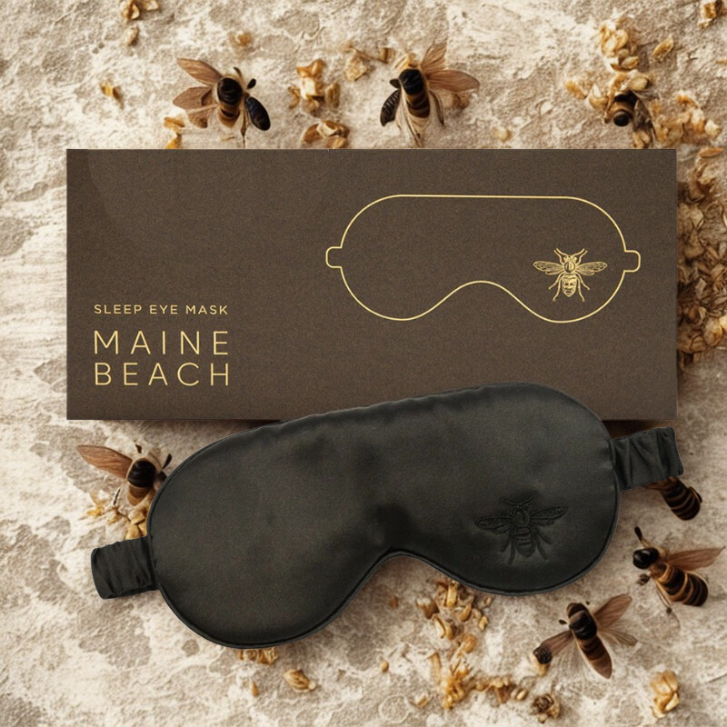 Sleep eye mask with 'Maine Beach' branding on a textured surface with bee decorations.