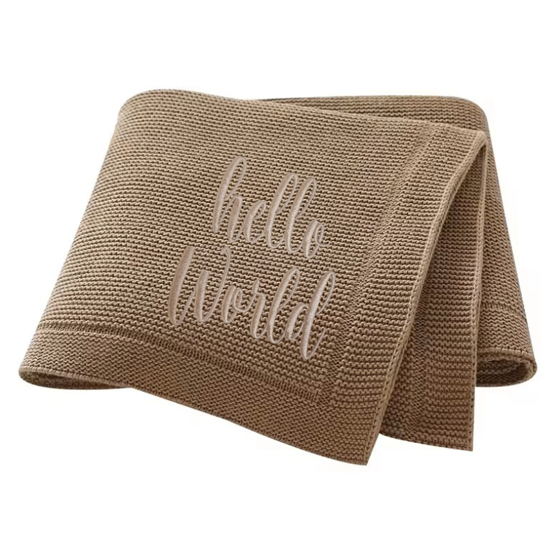 Brown knitted baby blanket with 'hello world' embroidery on a white background