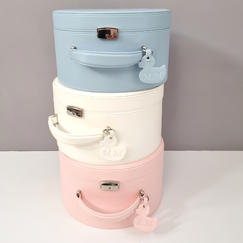 Stack of three pastel-colored cylindrical suitcases on a white surface with a gray background