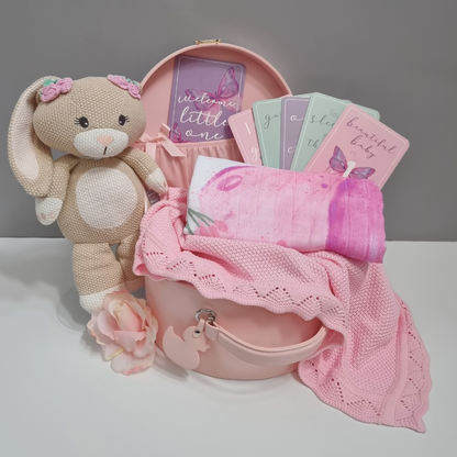 Pink baby gift set with teddy bear, cards, and blanket on a white surface.