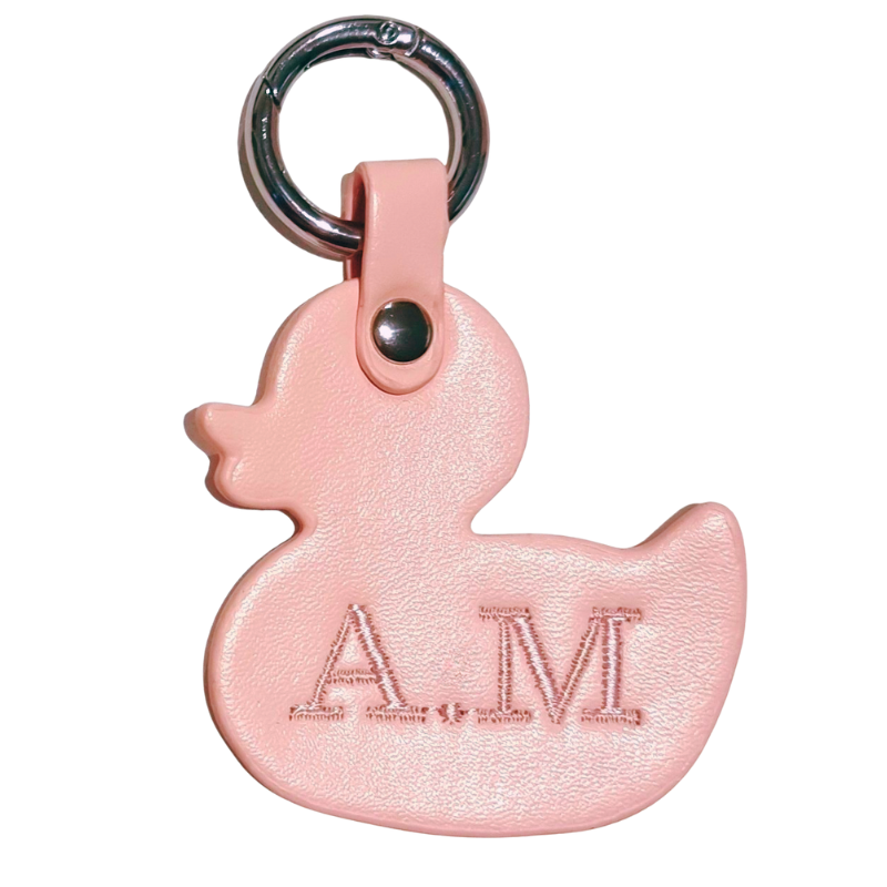 Pink duck-shaped keychain with 'AM' initials embroidered on a white background
