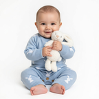 Baby in a blue outfit holding a white plush toy against a white background