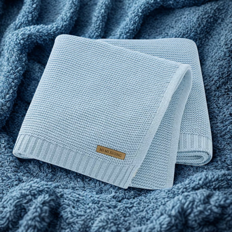 Light blue knitted blanket with a label on a textured blue background.