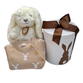 A baby gift hamper set including a beige and white knitted romper with bunny patterns, a beige plush bunny toy, and a white gift box with a bunny design and a brown ribbon.