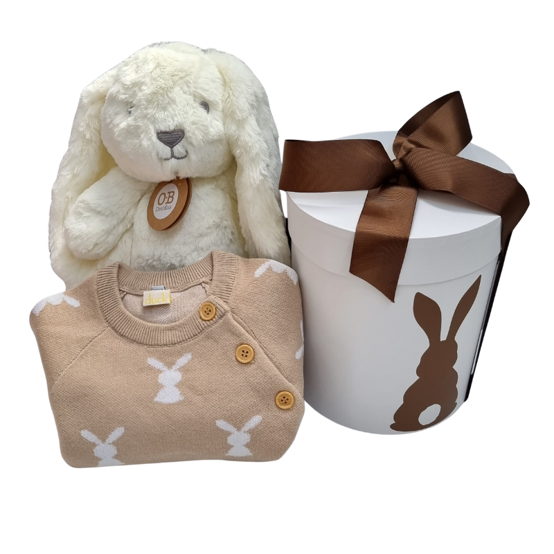 A baby gift hamper set including a beige and white knitted romper with bunny patterns, a beige plush bunny toy, and a white gift box with a bunny design and a brown ribbon.
