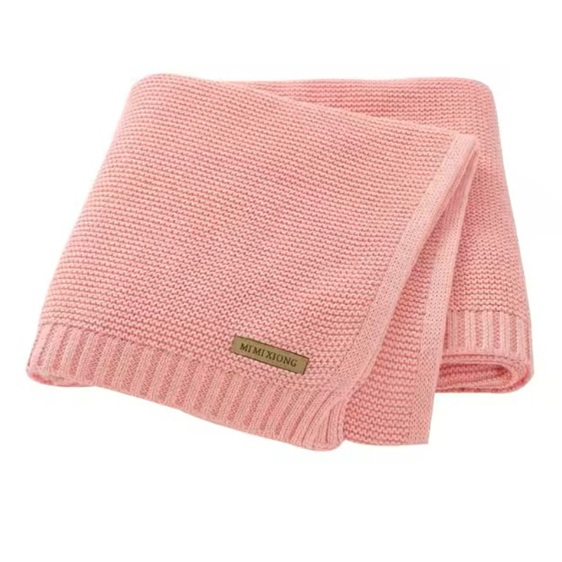 A folded knitted baby blanket in a light pink color, displayed on a white background