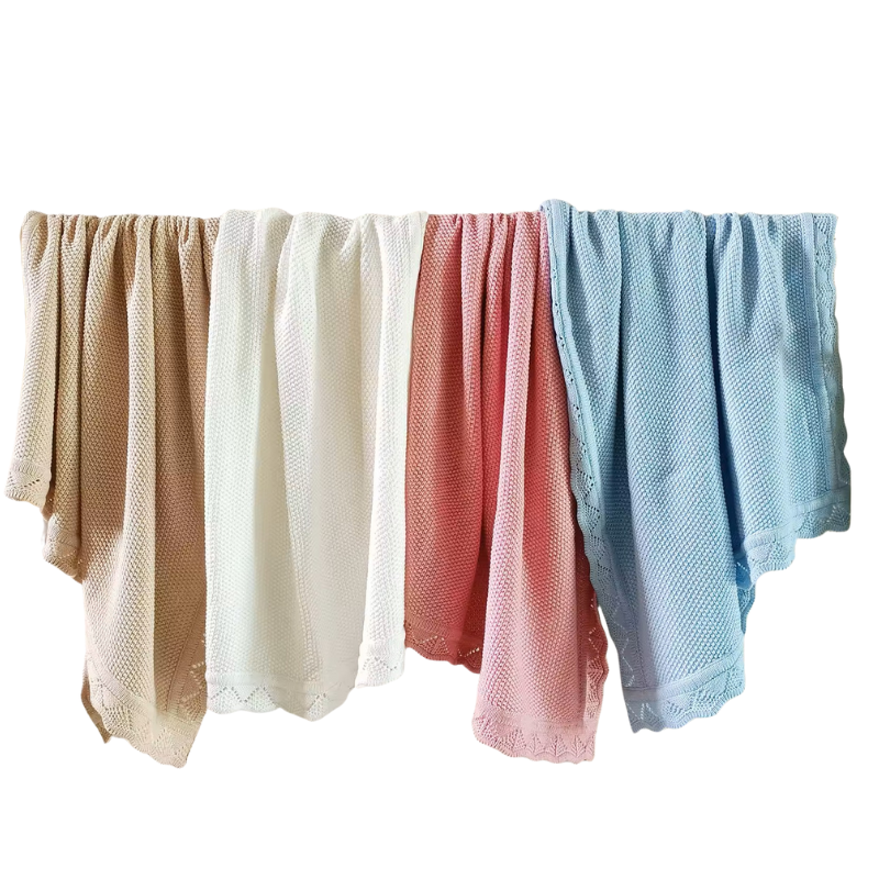 Four textured knitted baby blankets in oatmeal, white, pink and blue hanging side by side on a white background.