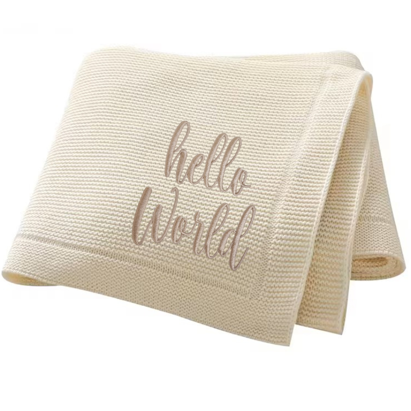Beige baby blanket with 'hello world' embroidered text on a white background