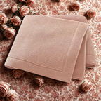 Folded pink knitted baby blanket on a floral background with roses.