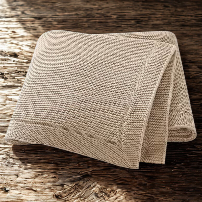 Beige knitted baby blanket on a wooden surface
