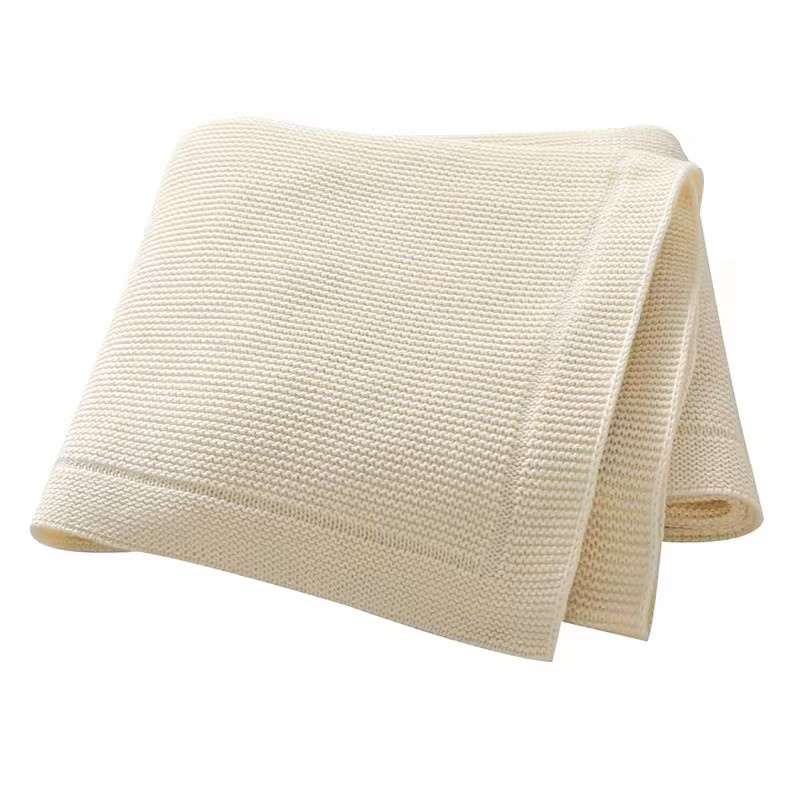 A folded beige knitted baby blanket with a solid line bordered edge, displayed on a white background