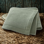 Knitted sage green baby blanket on a textured brown surface.