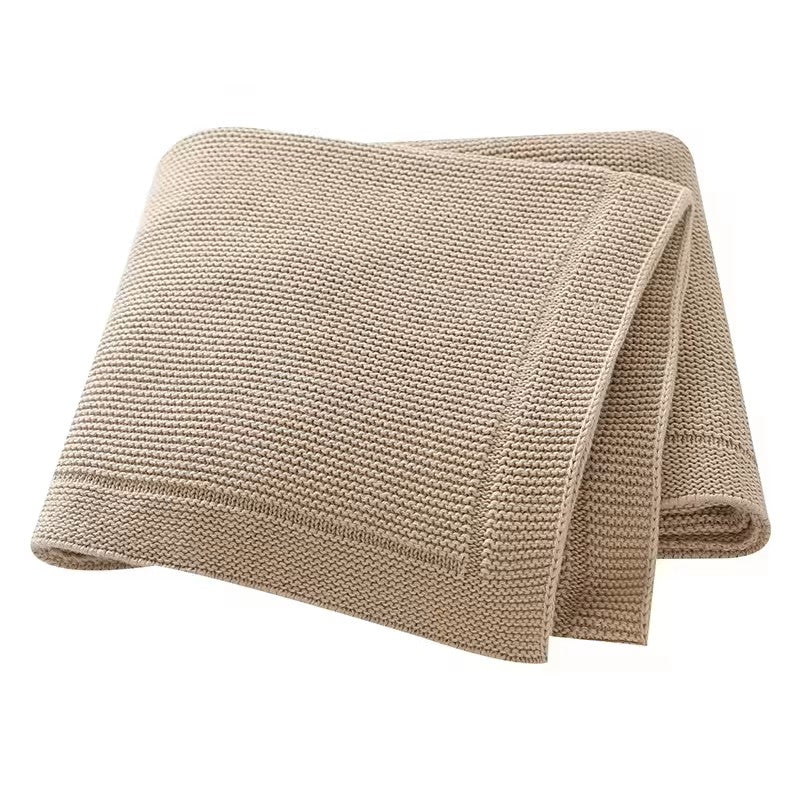 A folded beige knitted baby blanket with a solid line bordered edge, displayed on a white background