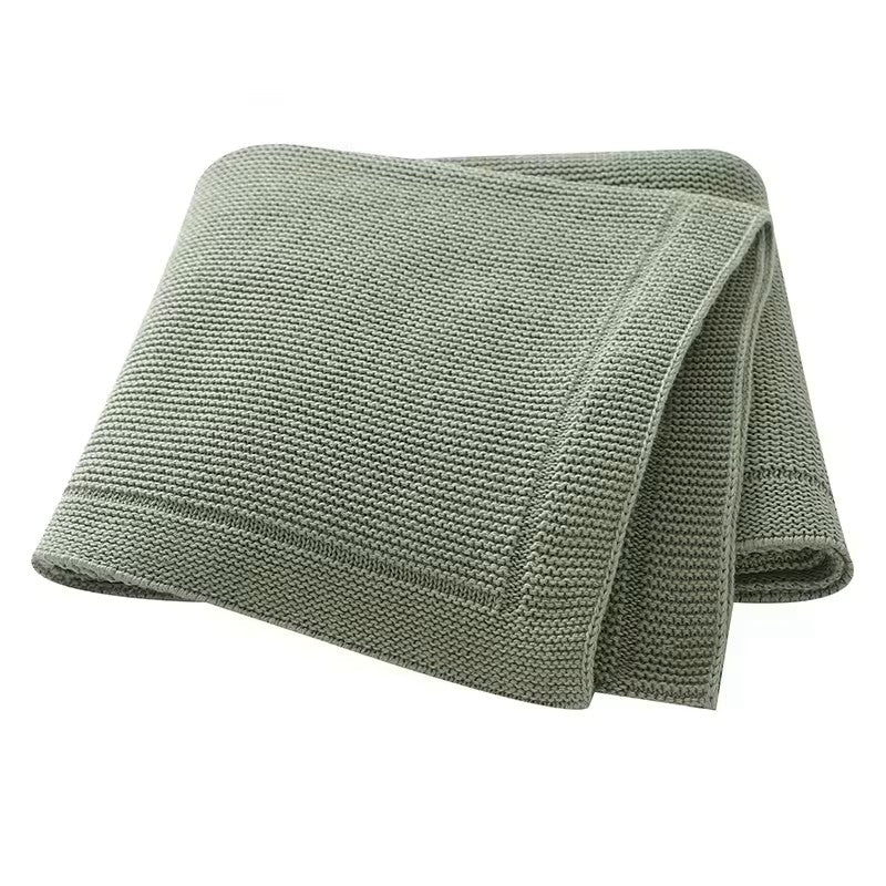 A folded beige knitted baby blanket with a solid line bordered edge, displayed on a white background