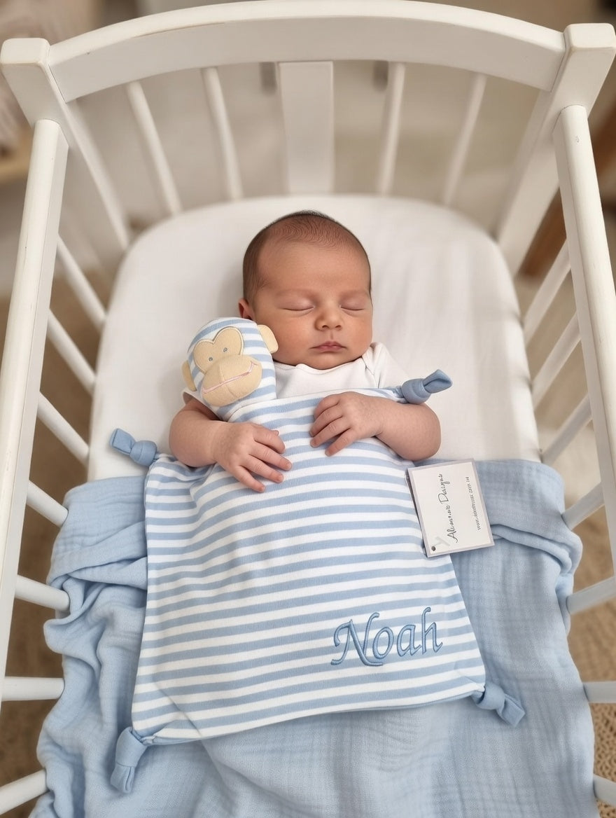 Newborn baby in a crib with blue and white striped blanket and teddy bear