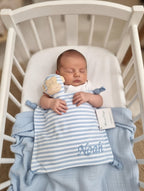 Newborn baby in a crib with blue and white striped blanket and teddy bear