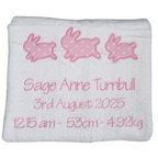 White blanket with pink embroidered bunnies and personalized text on a white background