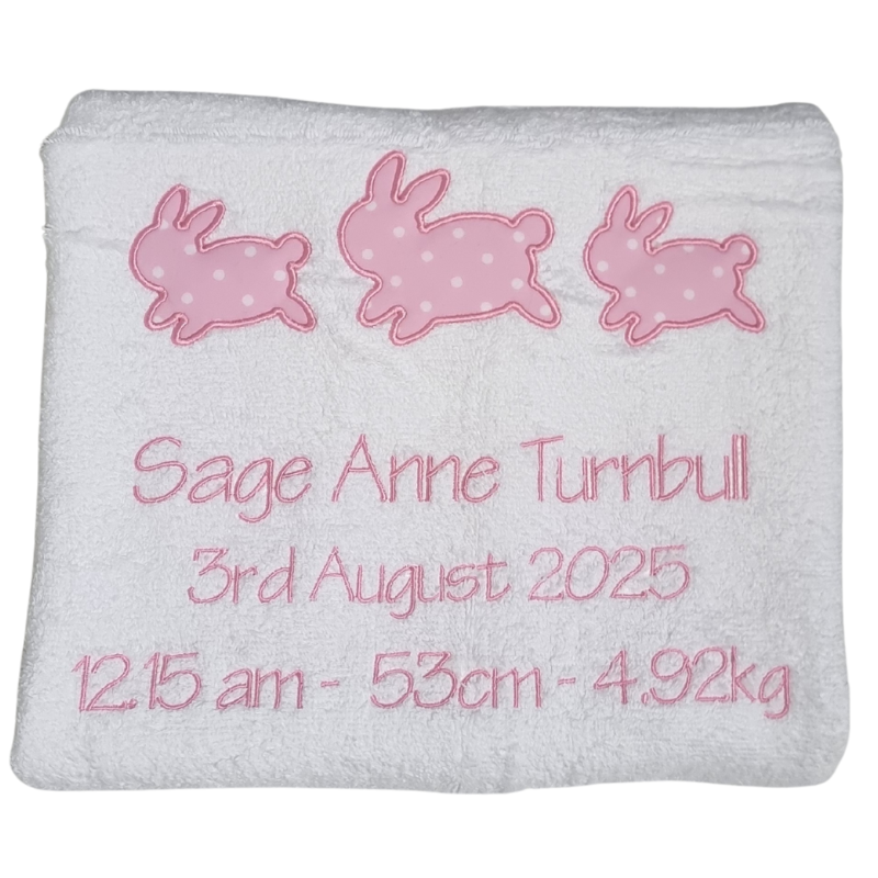 White blanket with pink embroidered bunnies and personalized text on a white background
