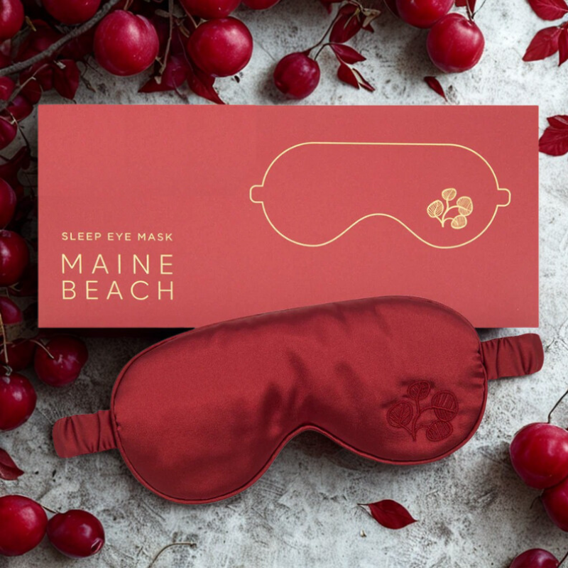 Red sleep eye mask with 'Maine Beach' branding on a surface with red berries.