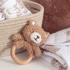 Teddy bear-shaped wooden rattle with baby blankets and a basket in the background