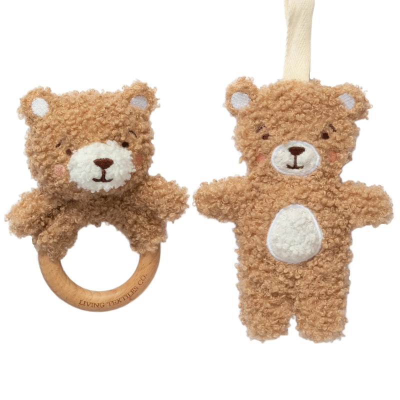Two teddy bear baby toys on a white background: one is a plush bear rattle with a wooden ring, and the other is a plush bear hanging toy with a cream fabric loop.