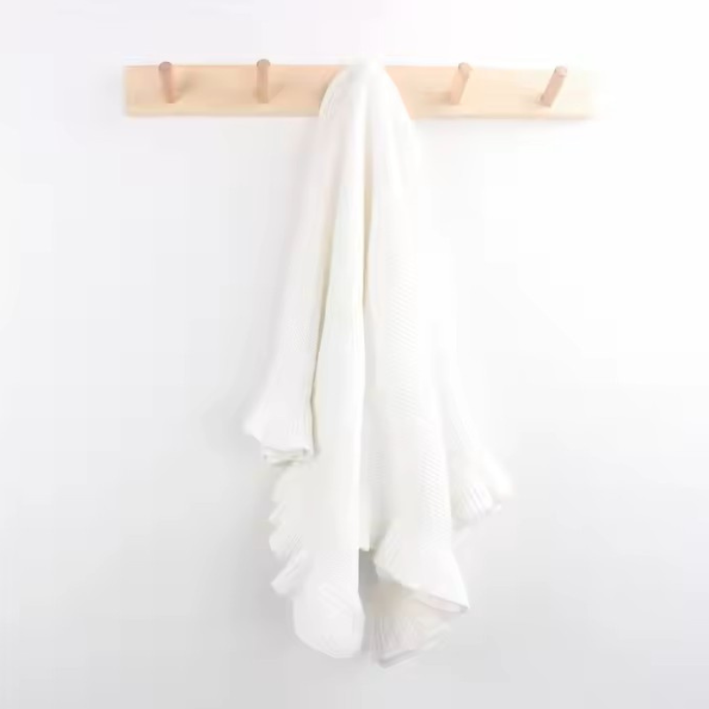 White knitted baby blanket hanging on a wooden rack against a white background