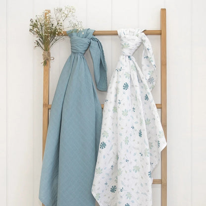 2 piece organic muslin sage green banana leaf design baby swaddle hanging on a rack