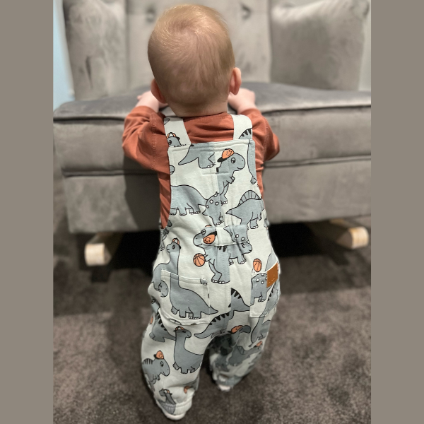 baby wearing dinosaur overalls by Hux baby