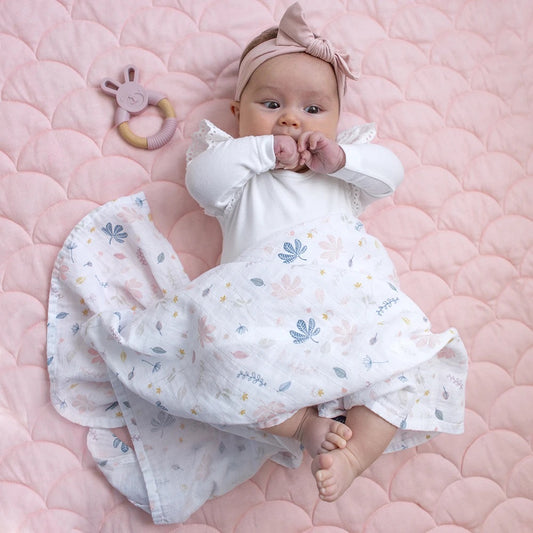 Baby wrapped in organic muslin pink botanical leaf design baby swaddle with silicone and wooden bunny teether.